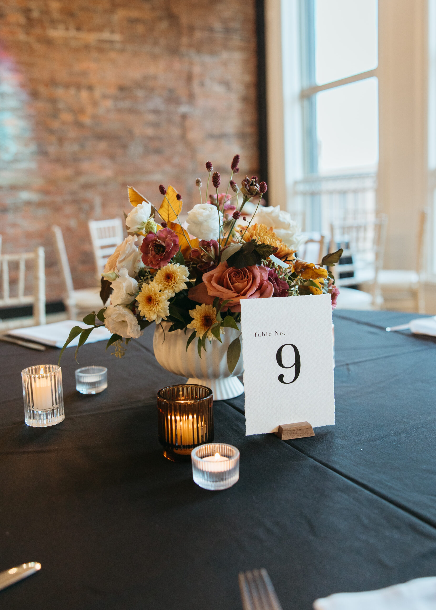 Elegant wedding reception table setting at Loft 214 in Stillwater, MN, featuring white linens, gold accents, and greenery centerpieces against an exposed brick wall