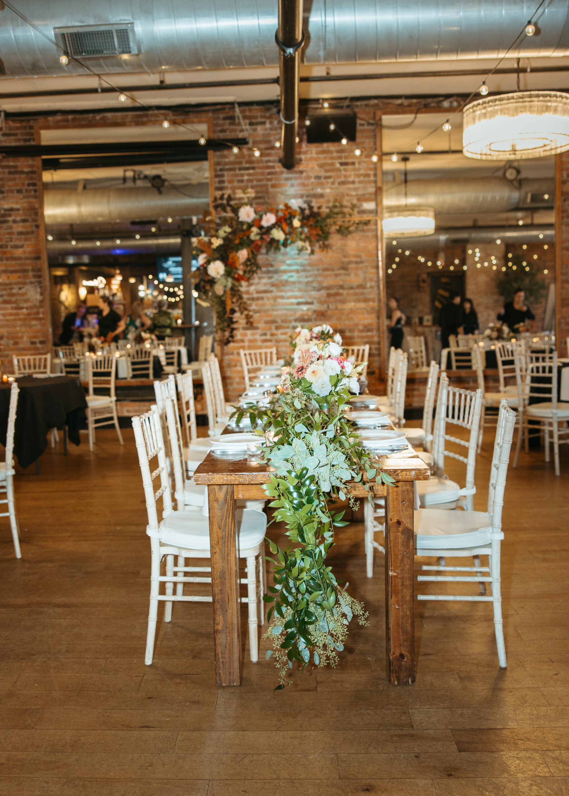 Elegant wedding reception table setting at Loft 214 in Stillwater, MN, featuring white linens, gold accents, and greenery centerpieces against an exposed brick wall