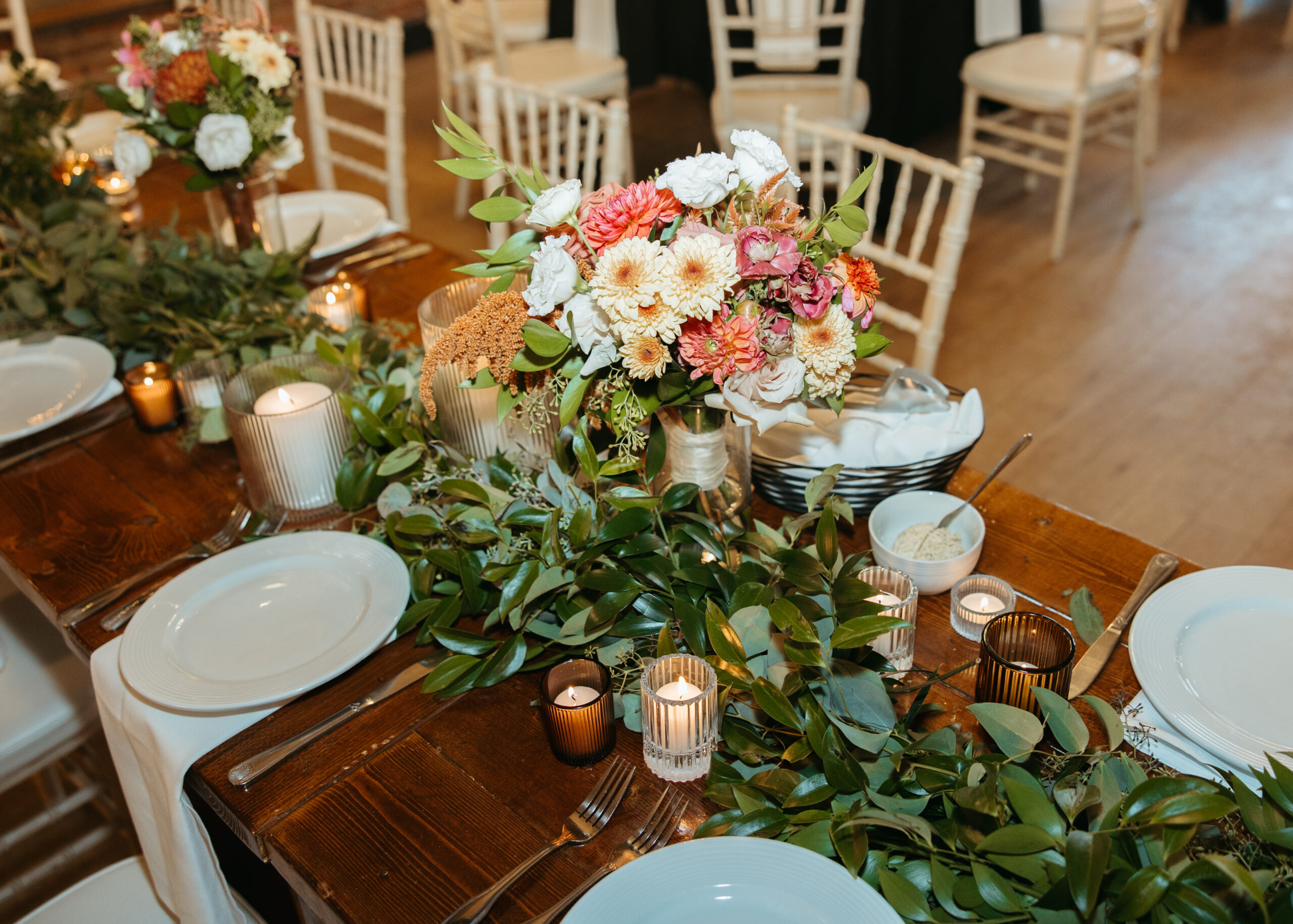 Elegant wedding reception table setting at Loft 214 in Stillwater, MN, featuring white linens, gold accents, and greenery centerpieces against an exposed brick wall