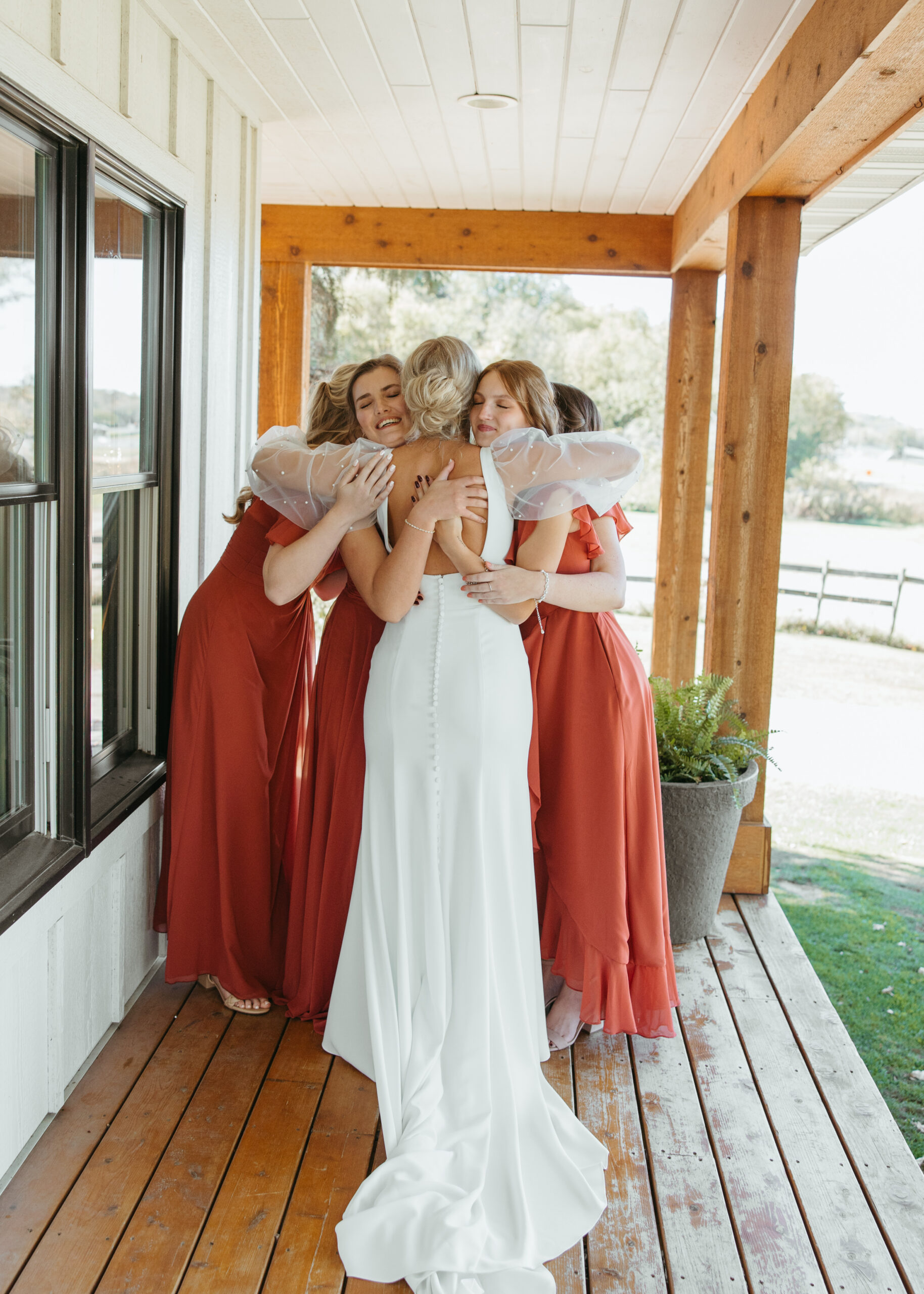 Candid photo of a bride in a fitted long-sleeve pearl wedding dress and her bridesmaids in terracotta dresses walking on the lawn at Genesis Ranch, captured by a Minneapolis wedding photographer.