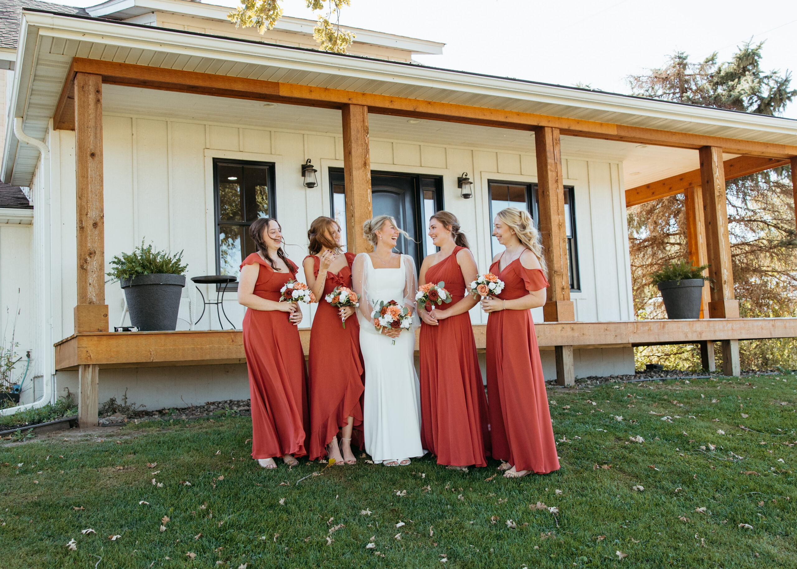 Candid photo of a bride in a fitted long-sleeve pearl wedding dress and her bridesmaids in terracotta dresses walking on the lawn at Genesis Ranch, captured by a Minneapolis wedding photographer.