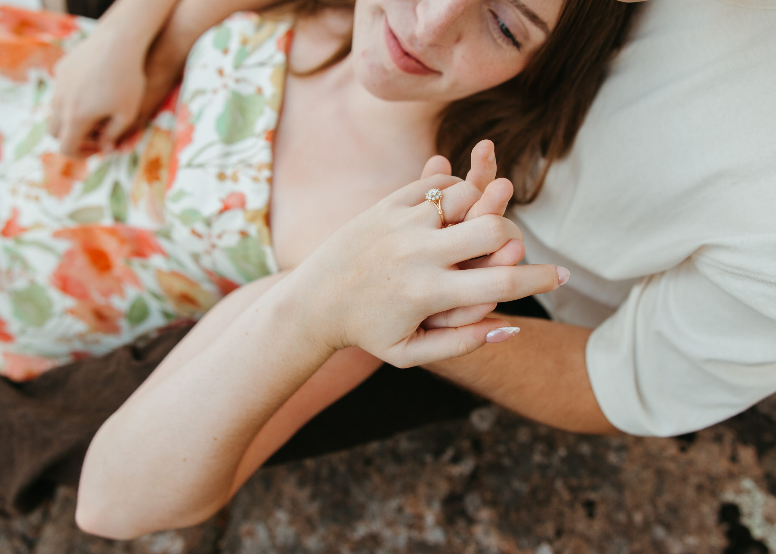 A couple holding hands and laughing on dark volcanic rocks along the North Shore shoreline, with the vast blue waters of Lake Superior stretching into the background.